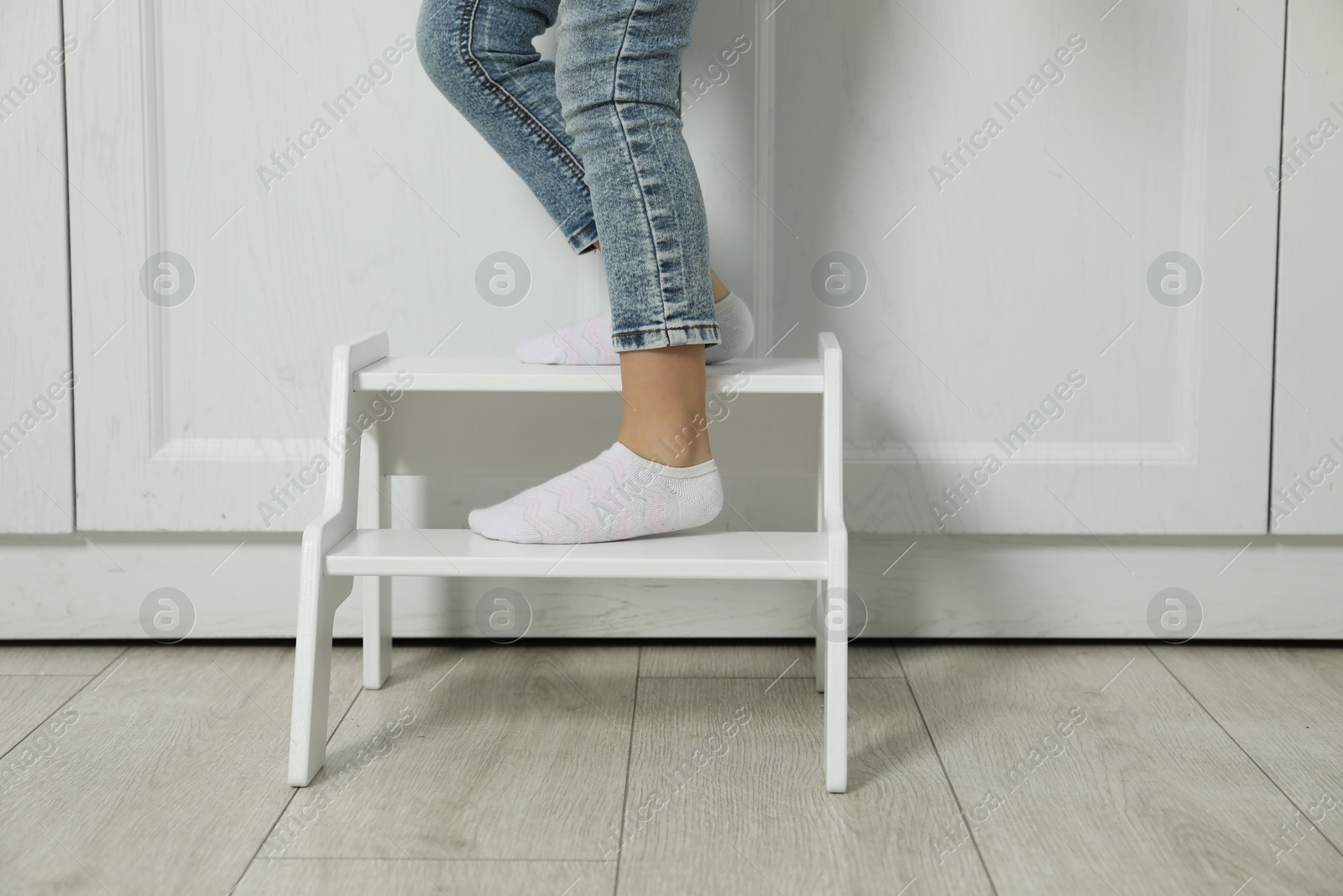 Photo of Little girl standing on step stool indoors, closeup