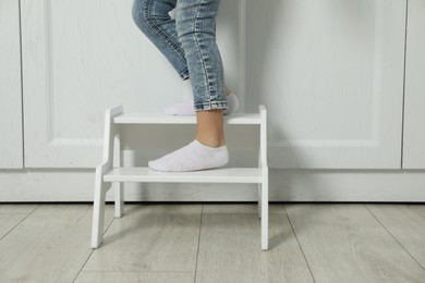 Photo of Little girl standing on step stool indoors, closeup