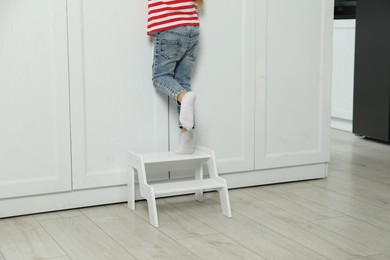 Photo of Little girl standing on step stool indoors, closeup