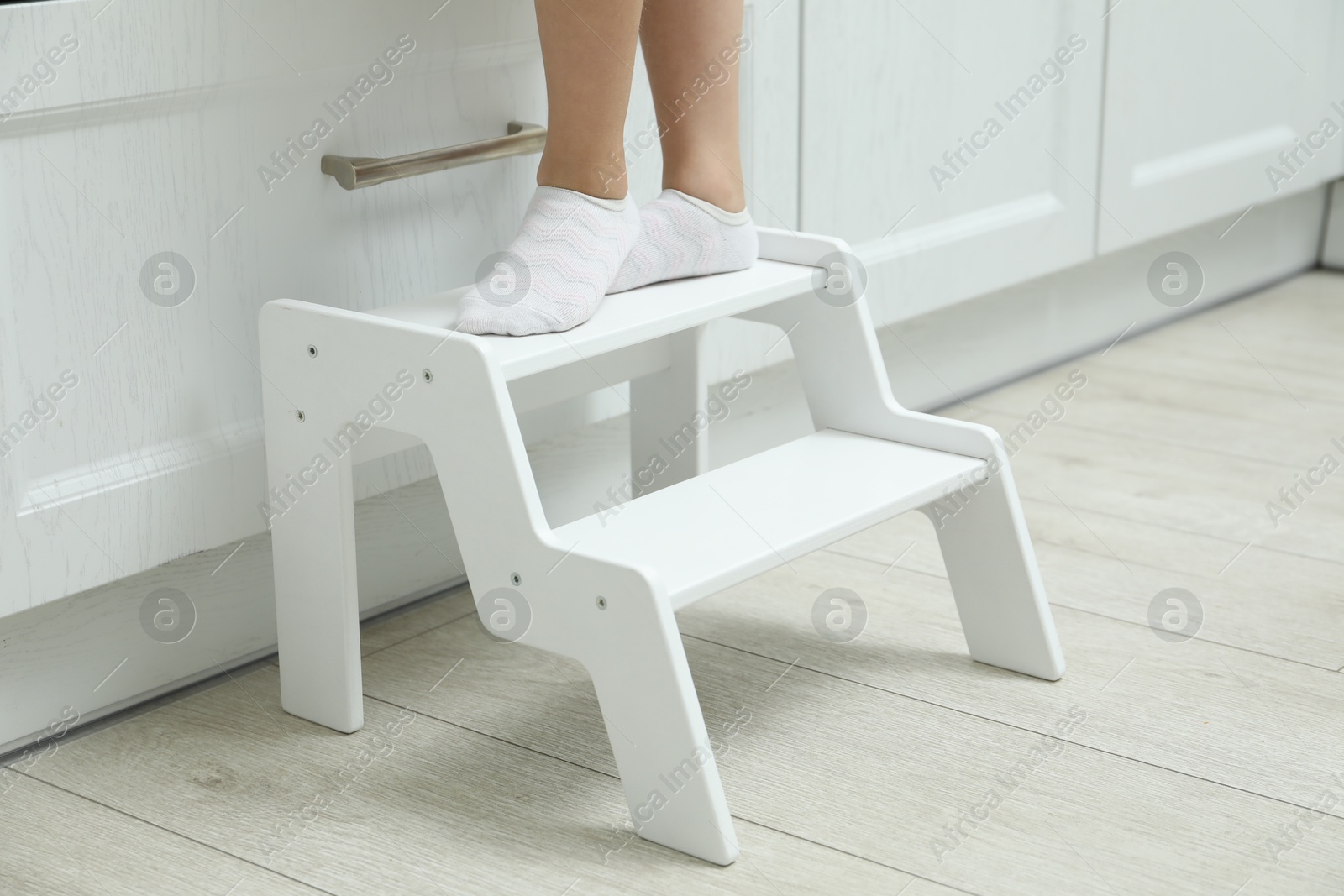 Photo of Little girl standing on step stool indoors, closeup