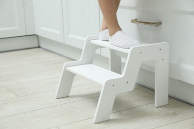 Photo of Little girl standing on step stool indoors, closeup