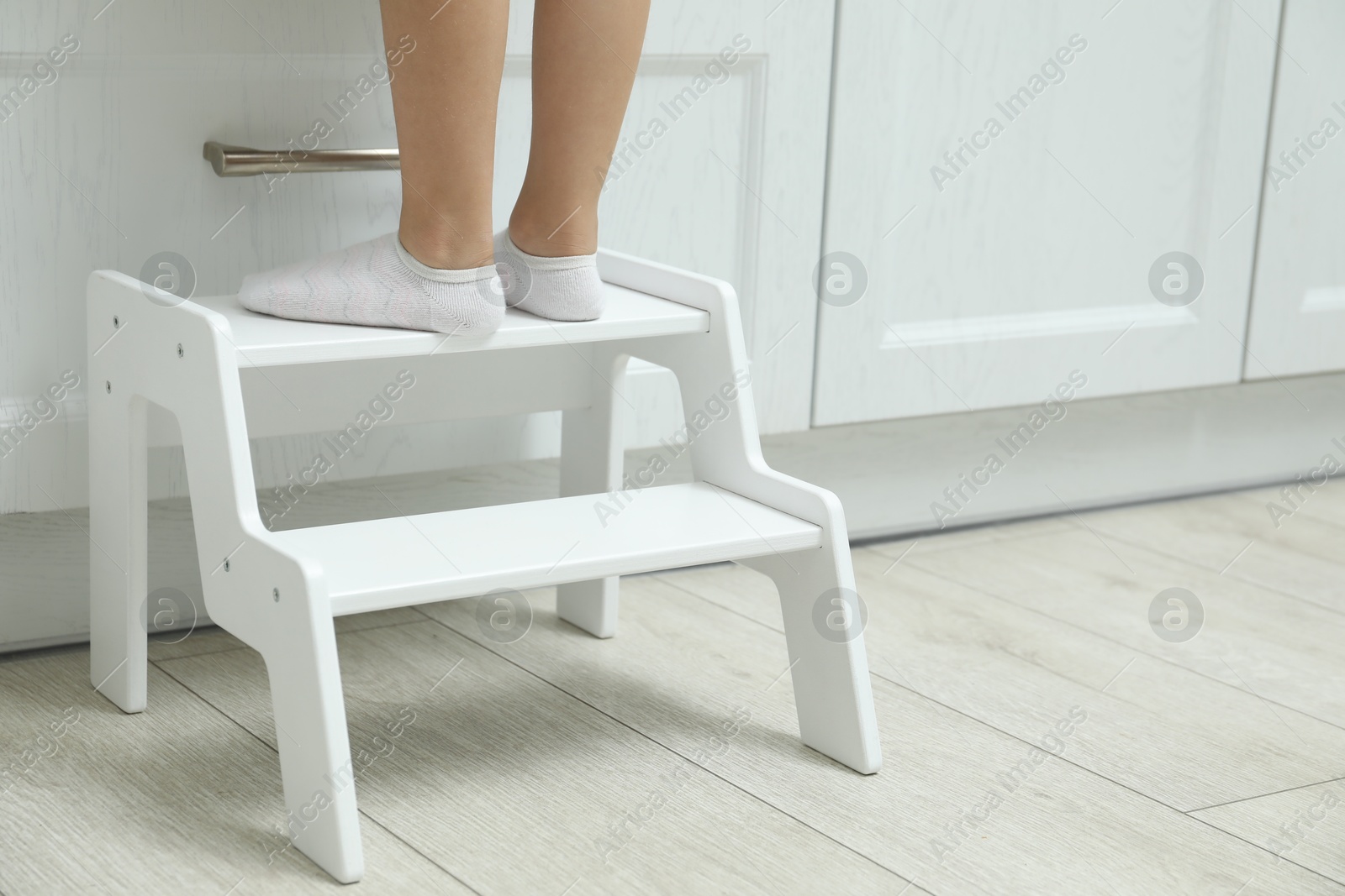 Photo of Little girl standing on step stool indoors, closeup