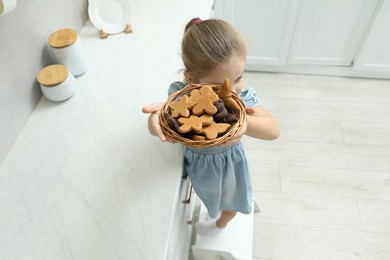 Photo of Little girl standing on step stool with bowl of cookies in kitchen, above view