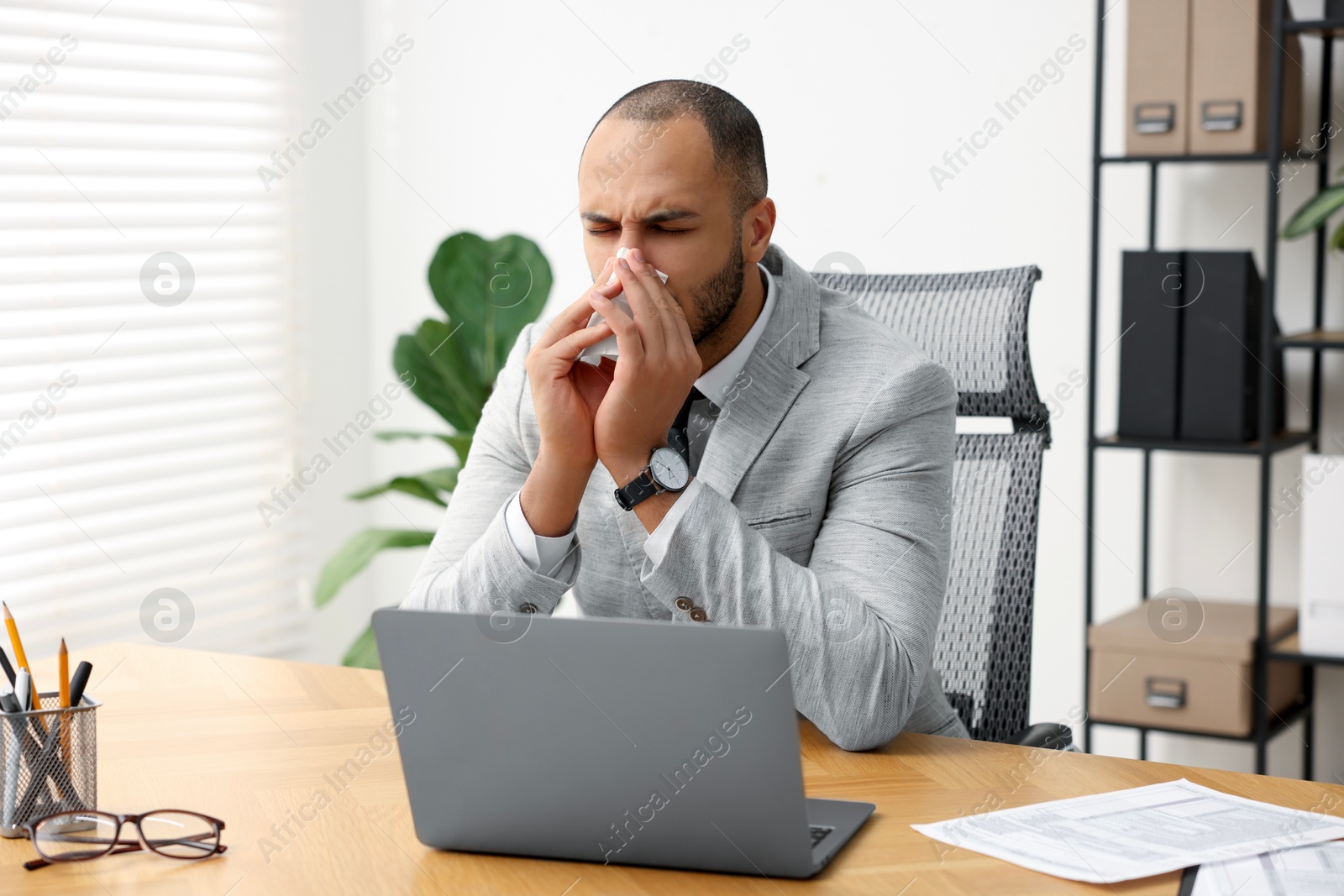 Photo of Sick man with runny nose at table in office