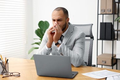 Photo of Sick man with runny nose at table in office