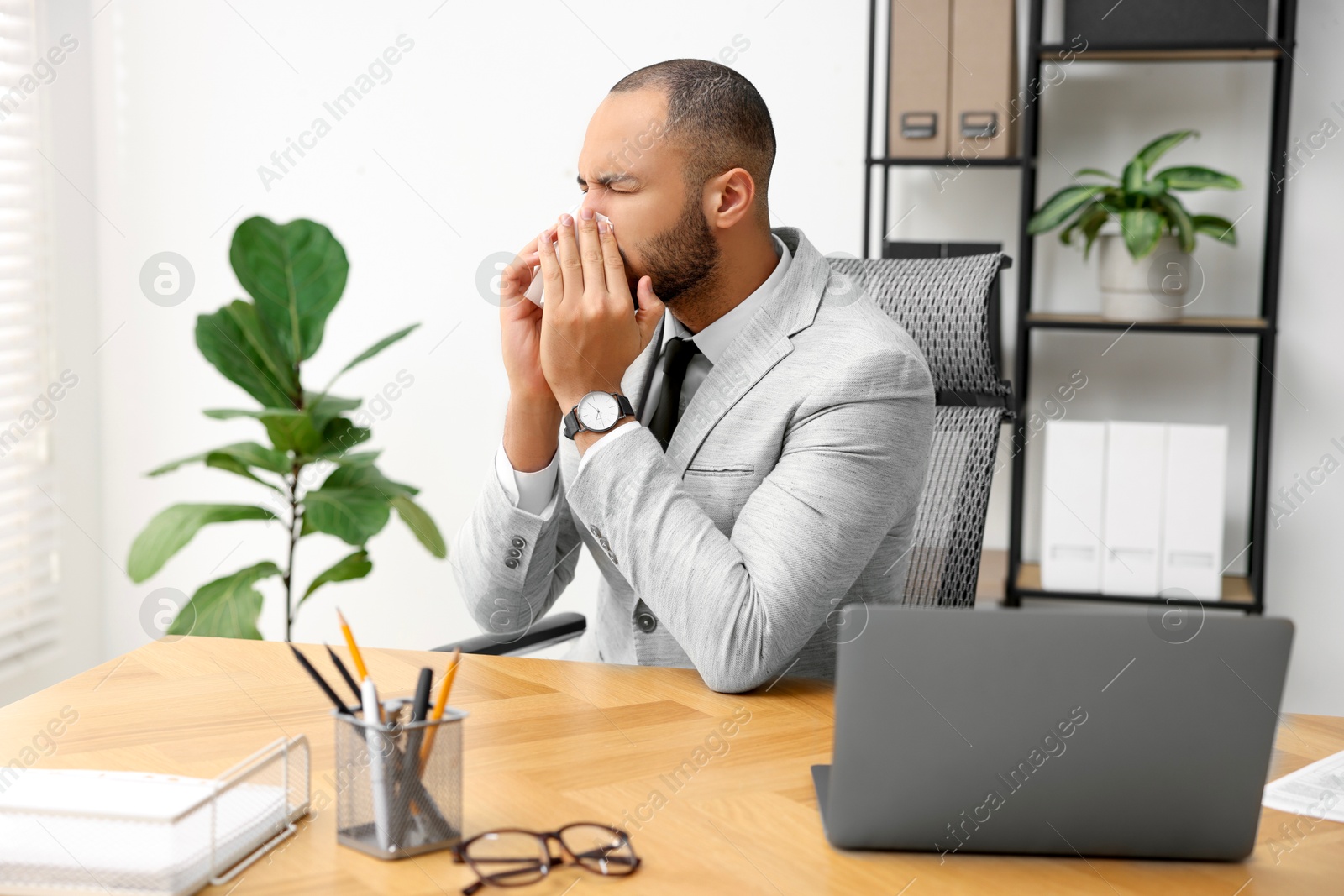 Photo of Sick man with runny nose at table in office