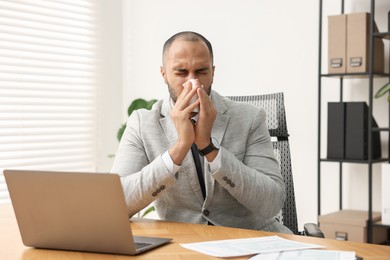 Photo of Sick man with runny nose at table in office