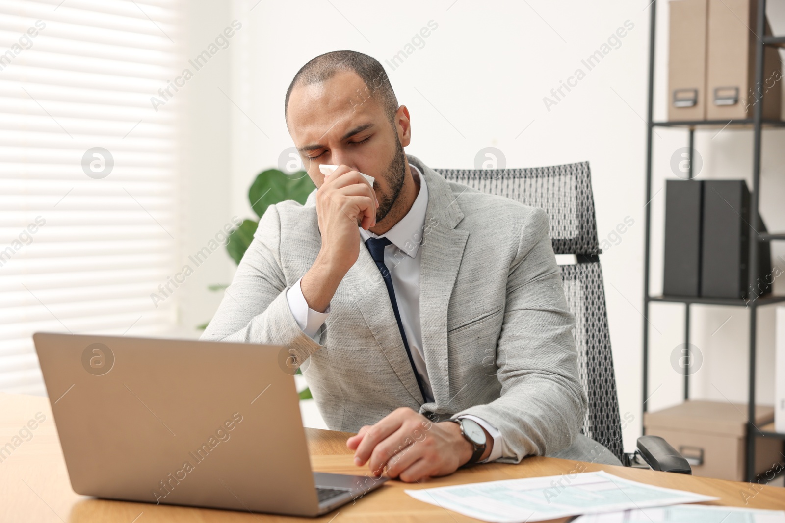 Photo of Sick man with runny nose at table in office