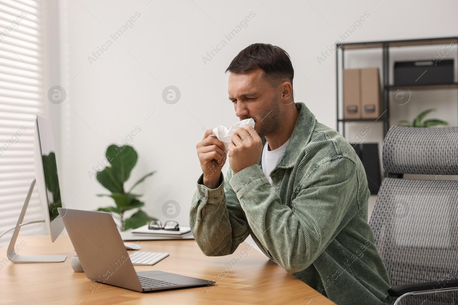 Photo of Sick man with runny nose at table in office