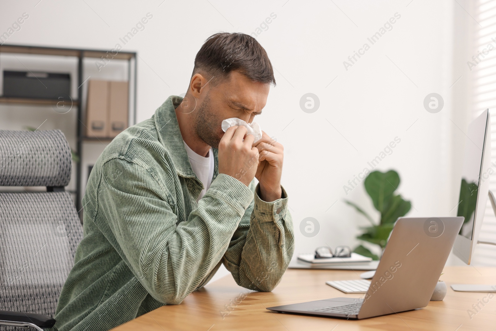 Photo of Sick man with runny nose at table in office