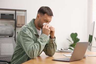 Sick man with runny nose at table in office