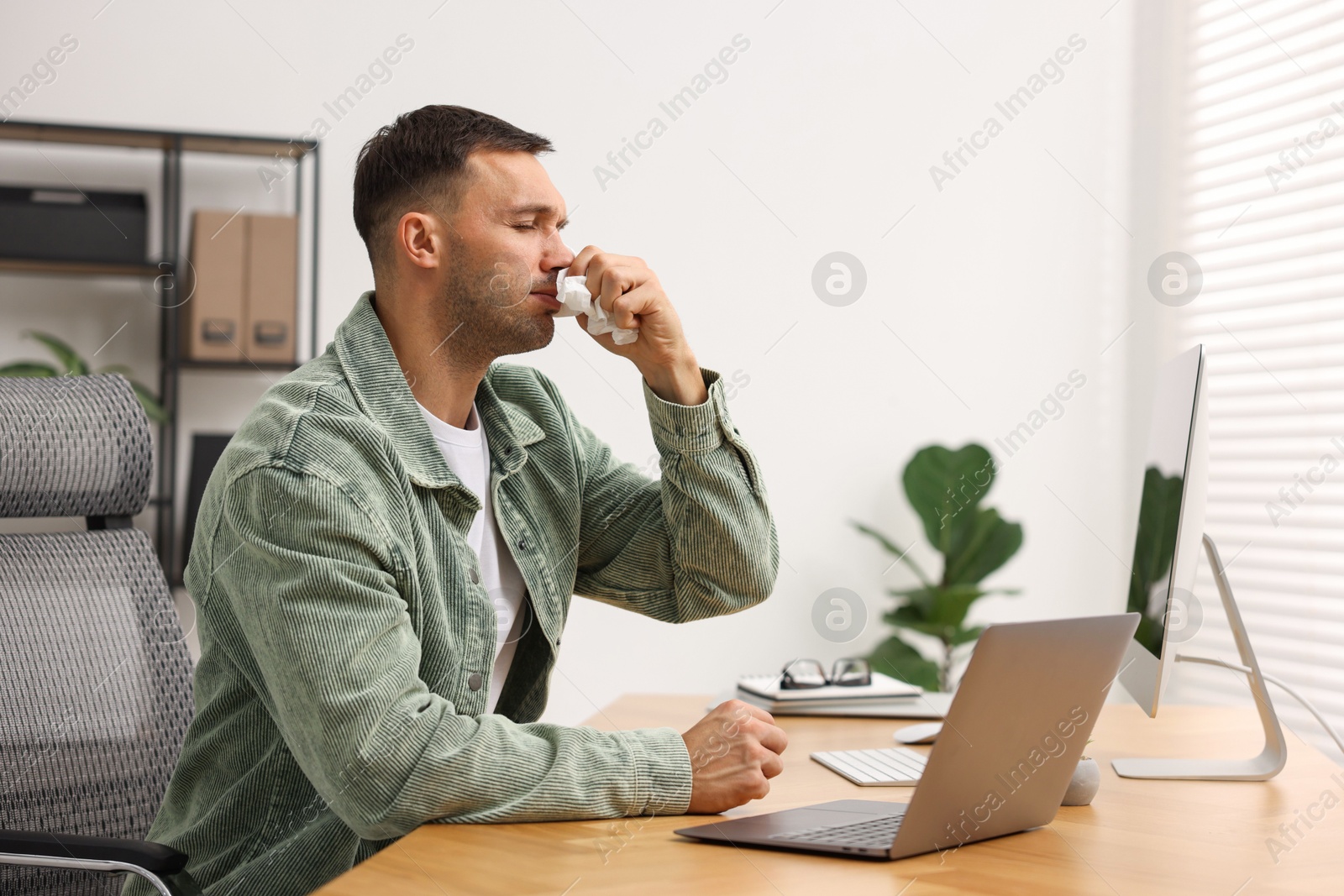 Photo of Sick man with runny nose at table in office