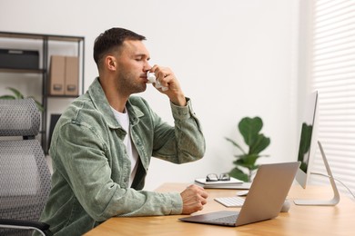 Sick man with runny nose at table in office