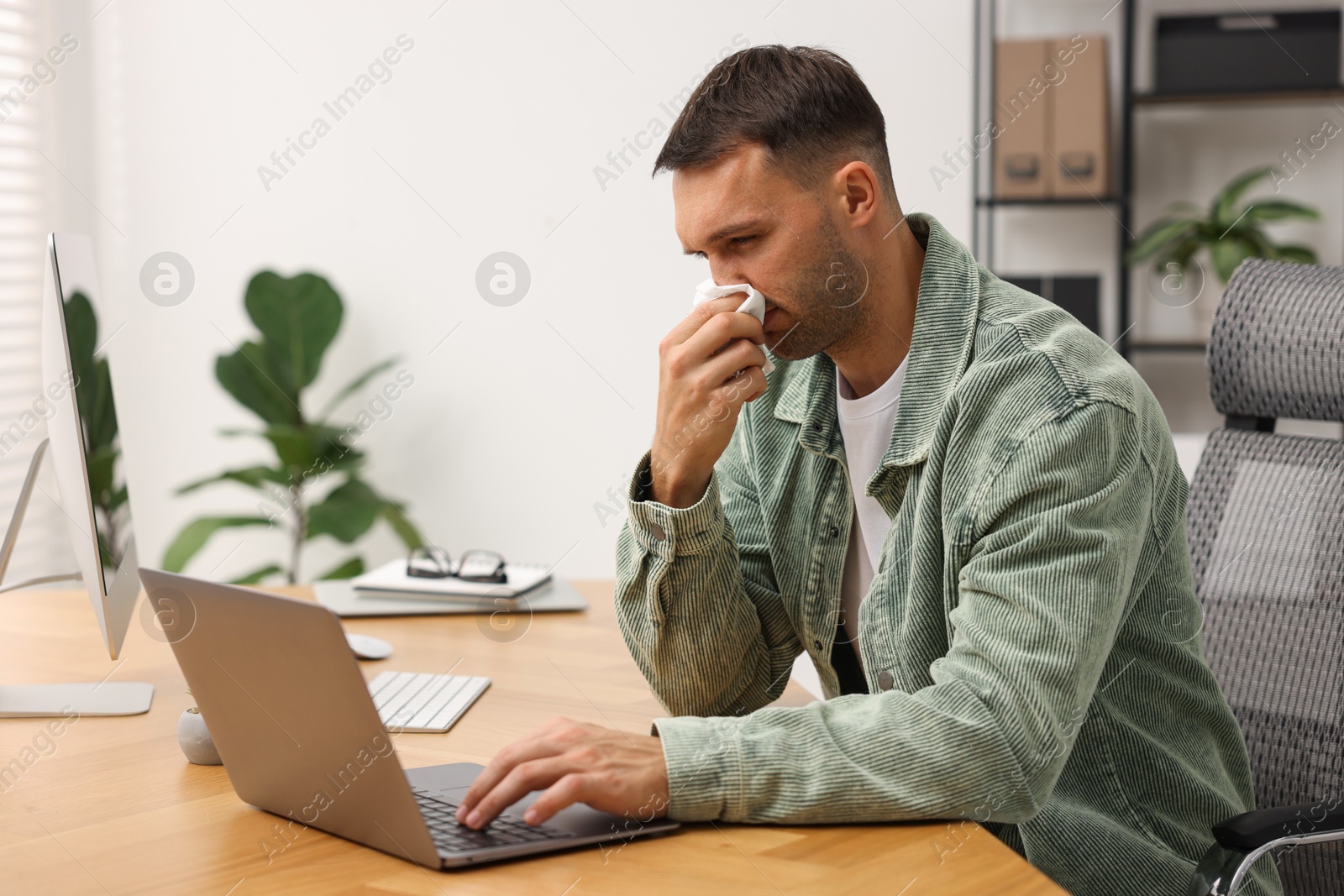 Photo of Sick man with runny nose at table in office