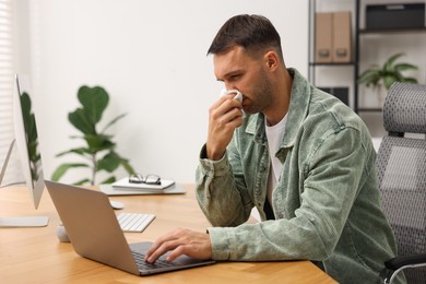 Sick man with runny nose at table in office