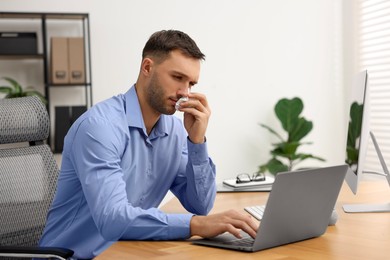 Photo of Sick man with runny nose at table in office