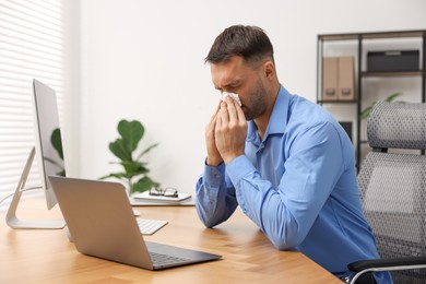 Photo of Sick man with runny nose at table in office