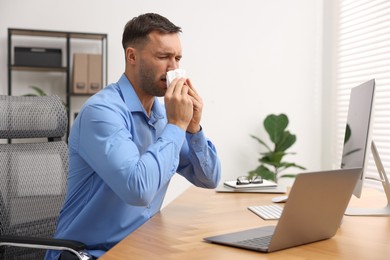 Sick man with runny nose at table in office