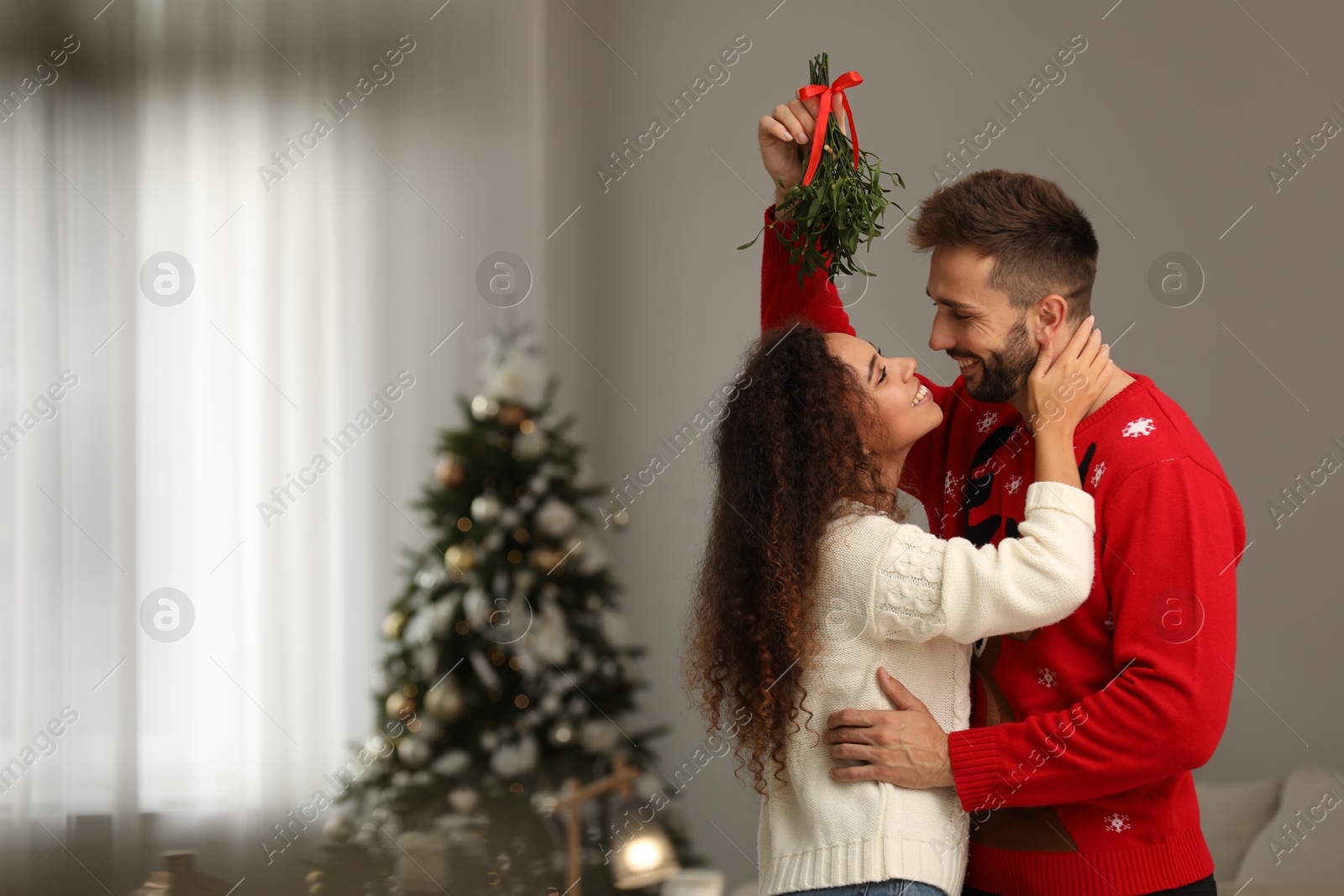 Photo of Lovely couple under mistletoe bunch in room decorated for Christmas