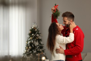 Photo of Lovely couple under mistletoe bunch in room decorated for Christmas