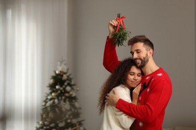 Photo of Lovely couple under mistletoe bunch in room decorated for Christmas