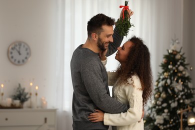 Lovely couple under mistletoe bunch in room decorated for Christmas