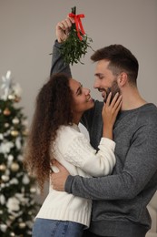 Lovely couple under mistletoe bunch in room decorated for Christmas