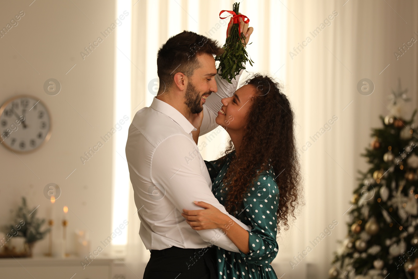 Photo of Lovely couple under mistletoe bunch in room decorated for Christmas