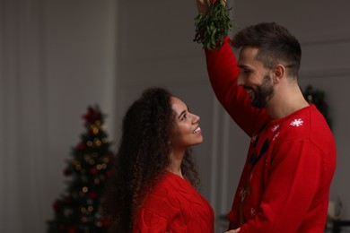 Photo of Lovely couple under mistletoe bunch in room decorated for Christmas