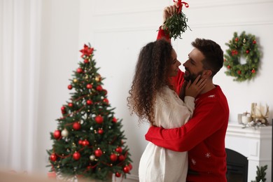 Lovely couple under mistletoe bunch in room decorated for Christmas