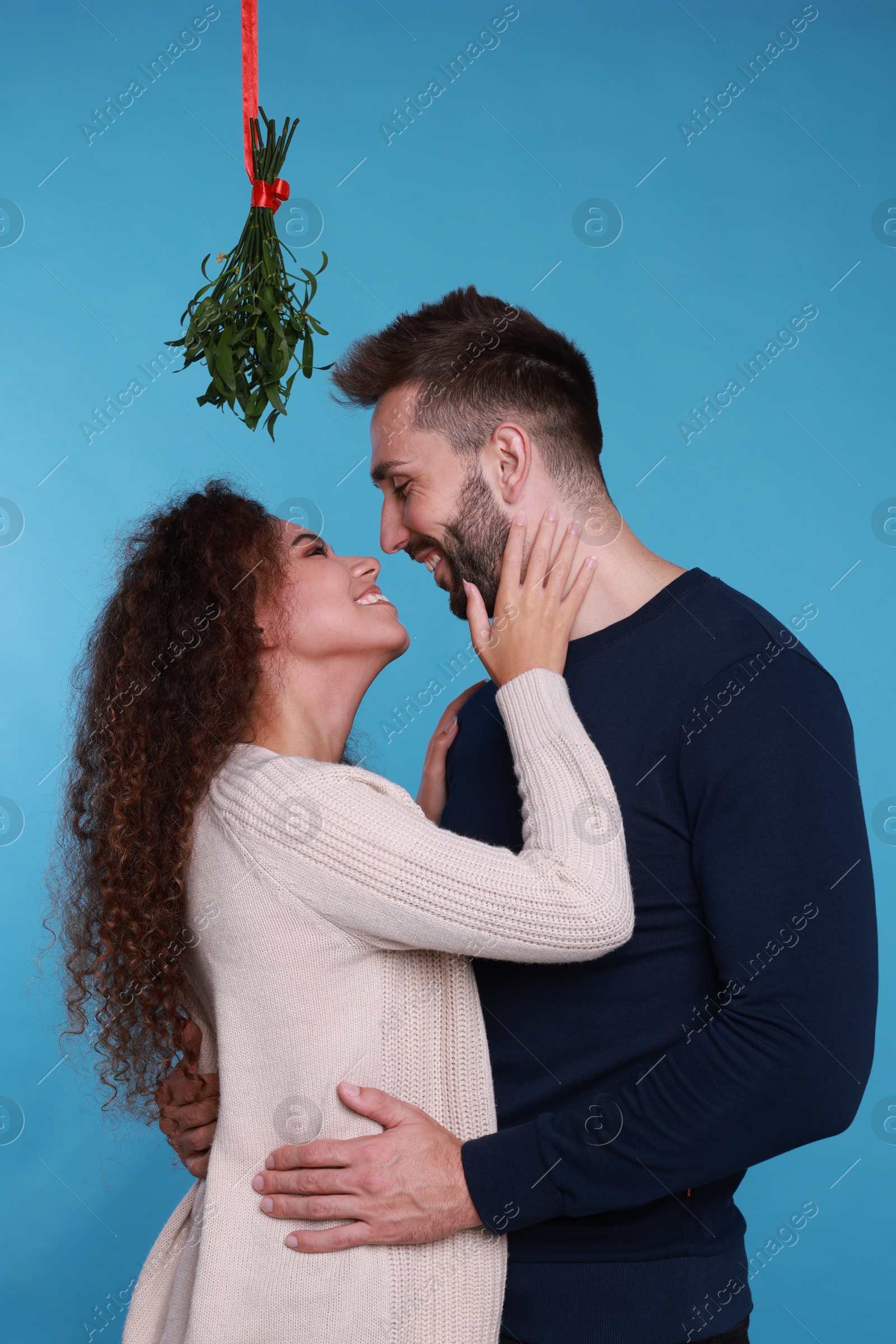 Photo of Lovely couple under mistletoe bunch on light blue background