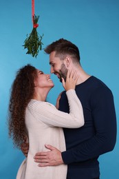 Photo of Lovely couple under mistletoe bunch on light blue background