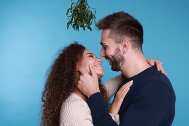 Photo of Lovely couple under mistletoe bunch on light blue background