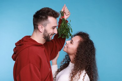 Lovely couple under mistletoe bunch on light blue background