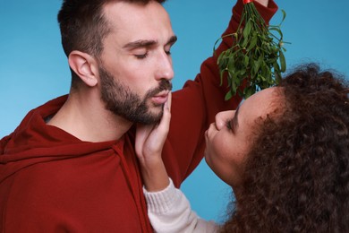 Photo of Lovely couple under mistletoe bunch on light blue background