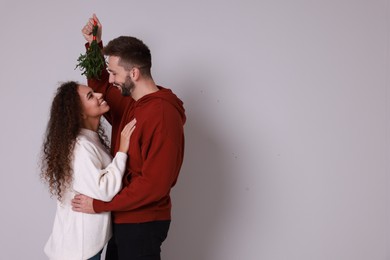 Lovely couple under mistletoe bunch on light grey background. Space for text