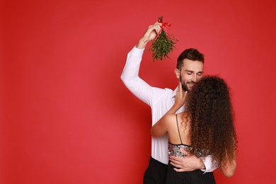 Photo of Lovely couple under mistletoe bunch on red background. Space for text