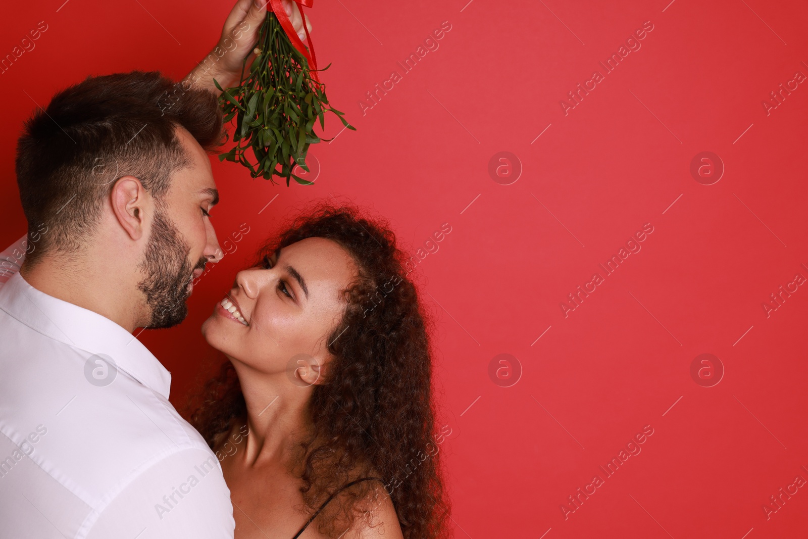 Photo of Lovely couple under mistletoe bunch on red background. Space for text