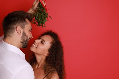 Photo of Lovely couple under mistletoe bunch on red background. Space for text