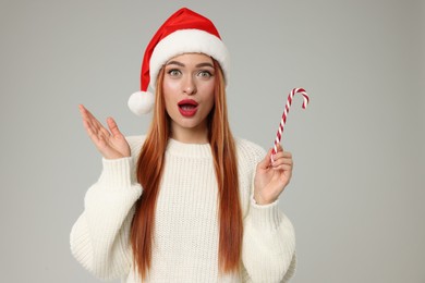 Photo of Emotional young woman in Santa hat with candy cane on light grey background. Christmas celebration