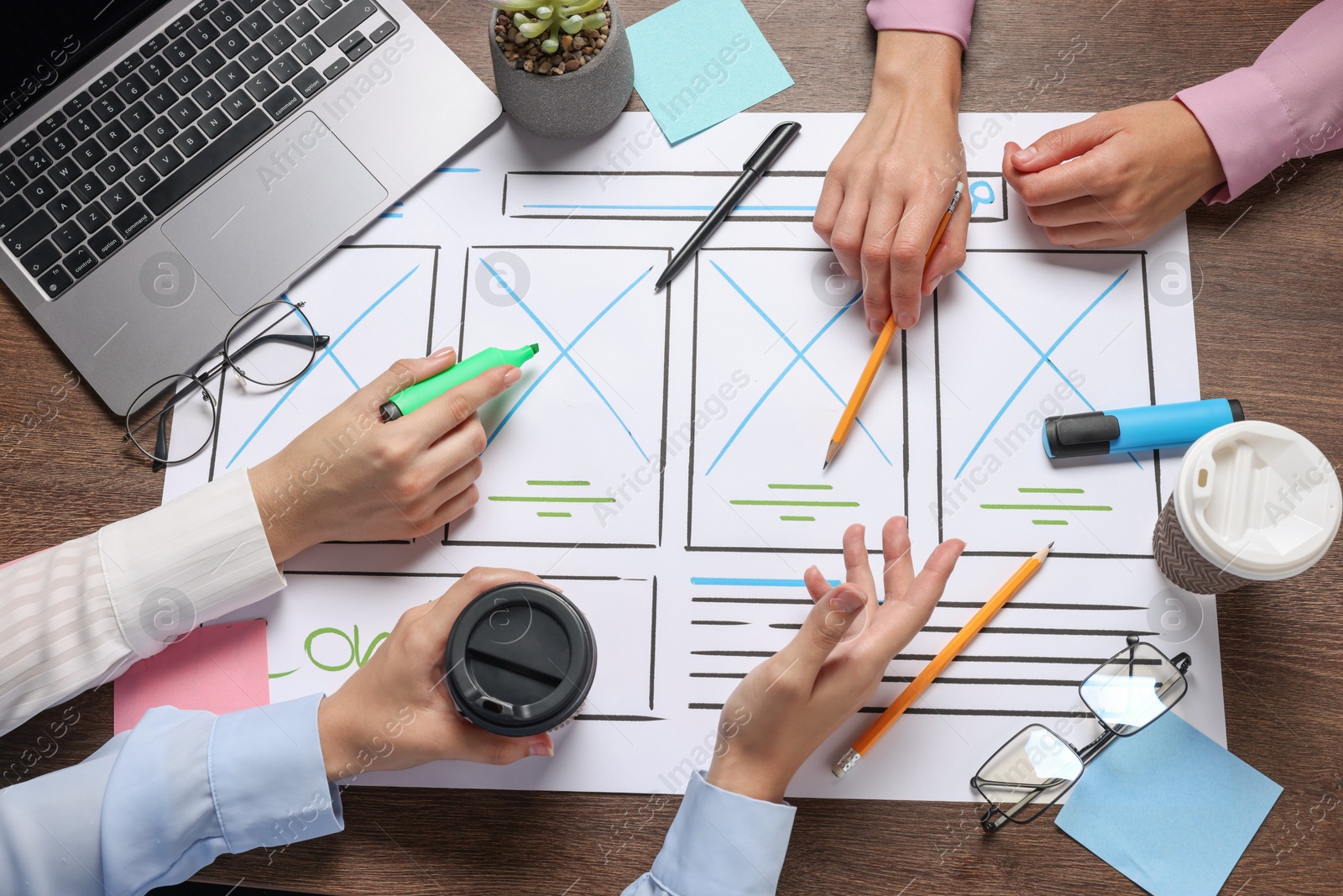 Photo of Developing UI design. Designers creating website wireframe on paper at wooden table, top view