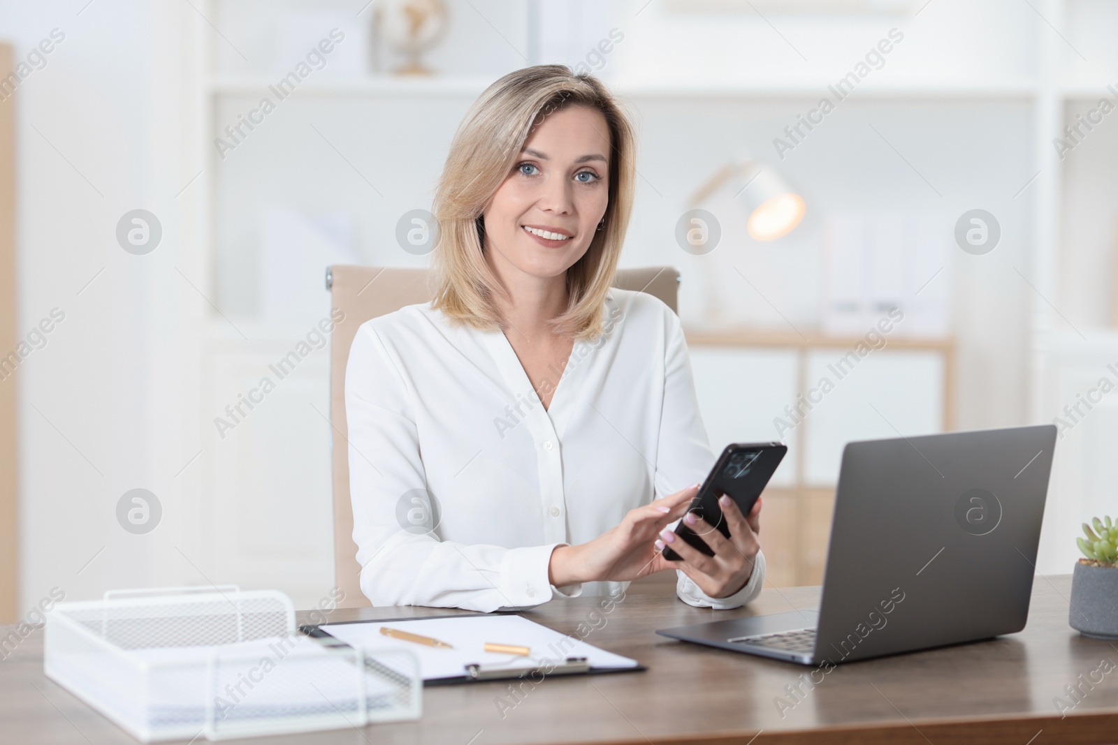 Photo of Businesswoman using smartphone at table in office