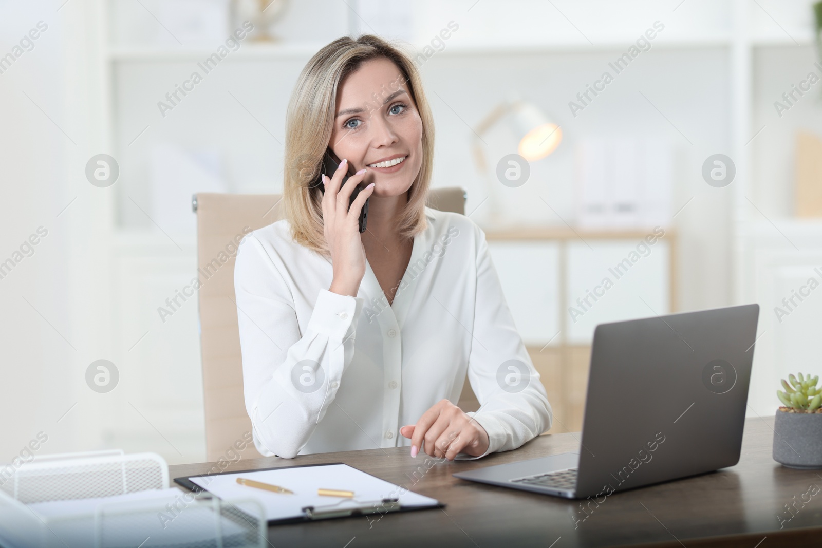 Photo of Businesswoman talking on smartphone at table in office