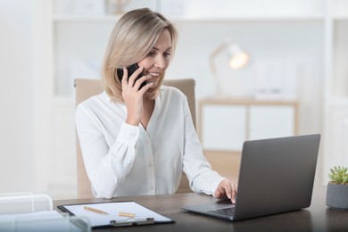 Photo of Businesswoman talking on smartphone at table in office