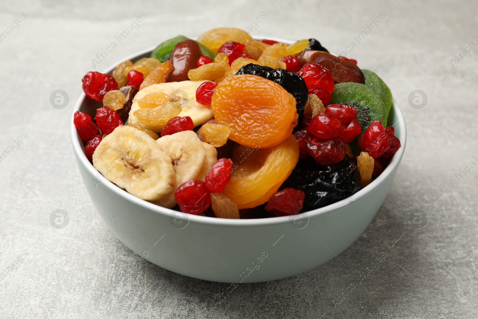 Photo of Mix of different dried fruits in bowl on gray textured table, closeup