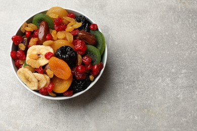 Photo of Mix of different dried fruits in bowl on gray textured table, top view. Space for text