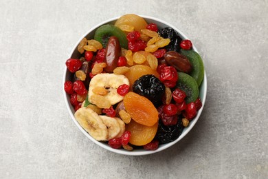 Photo of Mix of different dried fruits in bowl on gray textured table, top view