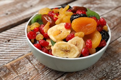 Photo of Mix of different dried fruits in bowl on wooden table, closeup