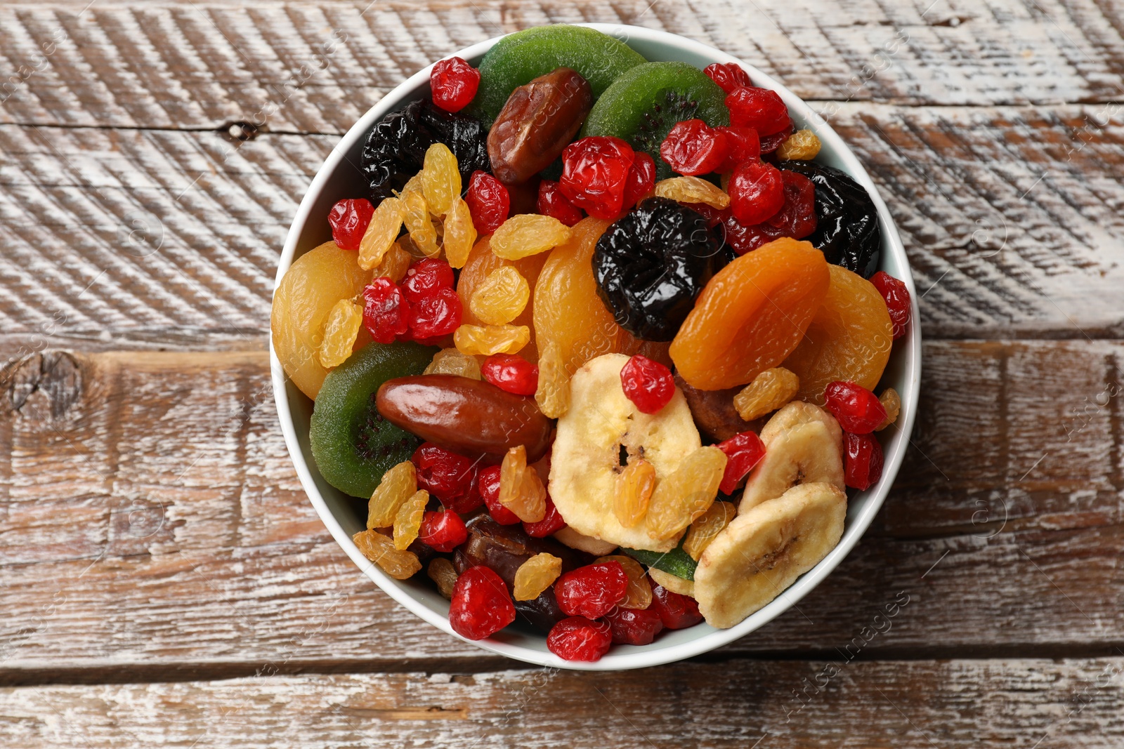 Photo of Mix of different dried fruits in bowl on wooden table, top view