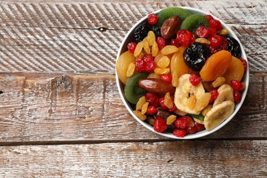 Photo of Mix of different dried fruits in bowl on wooden table, top view. Space for text